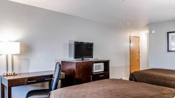 A hotel room with a desk, a television, a microwave, two beds, and a door.