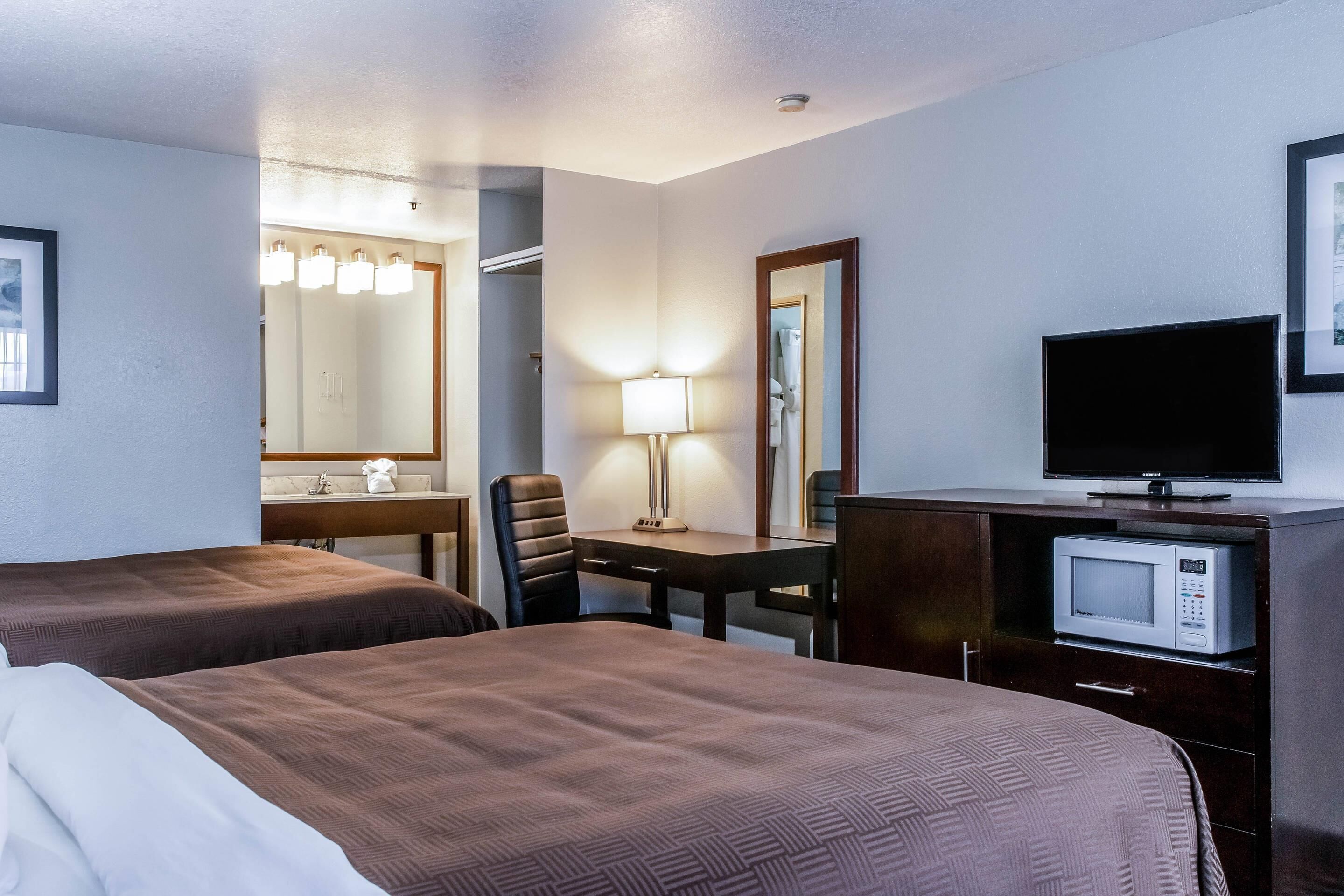 Ett hotellrum med två sängar, ett skrivbord med en lampa, en tv och en mikrovågsugn.