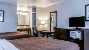 Ett hotellrum med två sängar, ett skrivbord med en lampa, en tv och en mikrovågsugn.