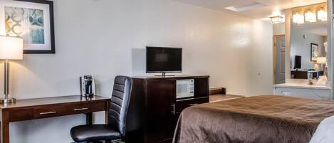 A hotel room with a bed, a desk with a chair, a television, a microwave, and a large mirror.