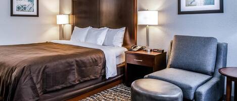 Habitación de hotel con una cama grande, dos lámparas de noche, una silla y una mesita.