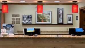 A hotel reception area with a check-in counter, digital kiosks, and framed artwork on the wall. - Country Inn & Suites by Radisson, Owatonna, MN (Owatonna)