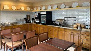 A modern kitchen with wooden cabinets, a granite countertop, and a dining area with wicker chairs. - Country Inn & Suites by Radisson, Owatonna, MN (Owatonna)