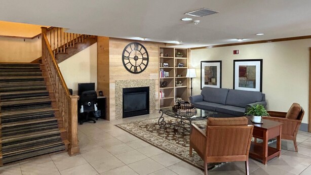 A spacious living area with a fireplace, a large clock, a staircase, and a seating area with a coffee table and chairs. - Country Inn & Suites by Radisson, Owatonna, MN (Owatonna)