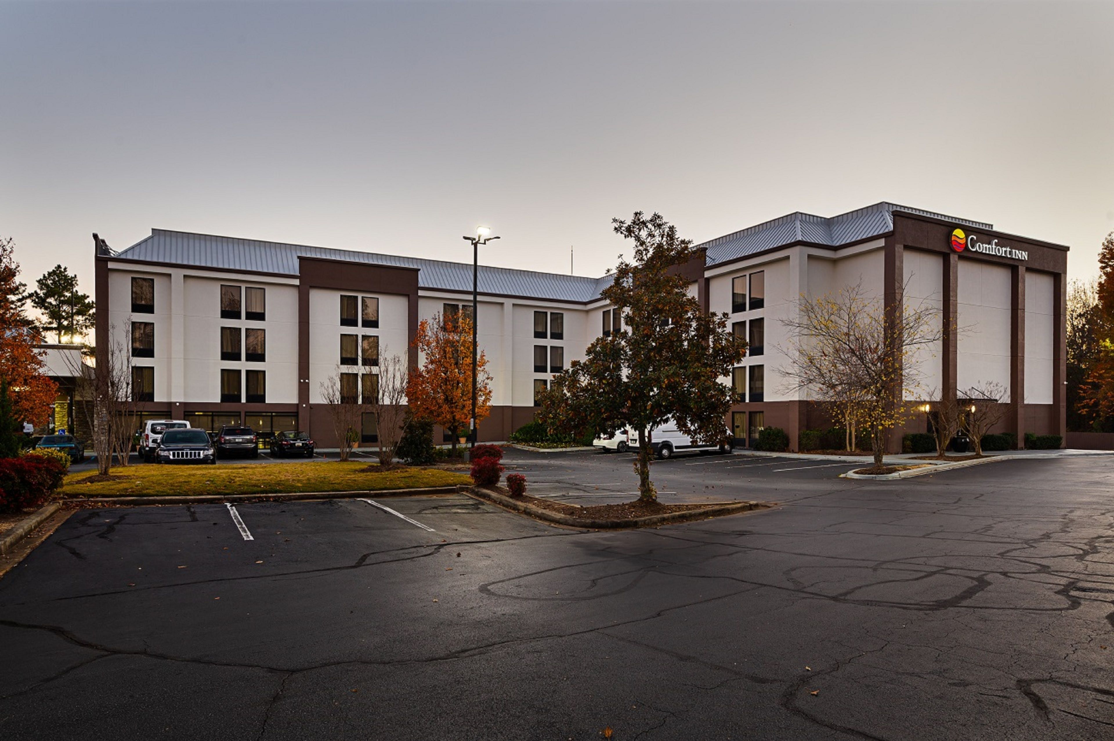 A Comfort Inn hotel with a parking lot, trees, and a clear sky.