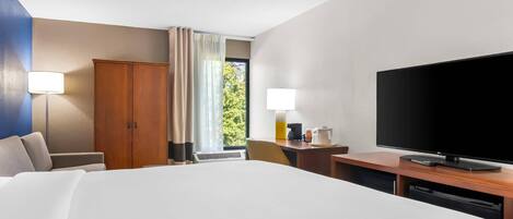 A hotel room with a large bed, a desk with a flat-screen TV, a wardrobe, and a window with curtains.