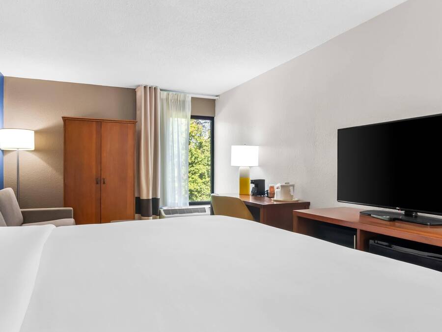 Quarto de hotel com uma cama grande, uma escrivaninha, televisão de tela plana, guarda-roupa e janela com cortinas.