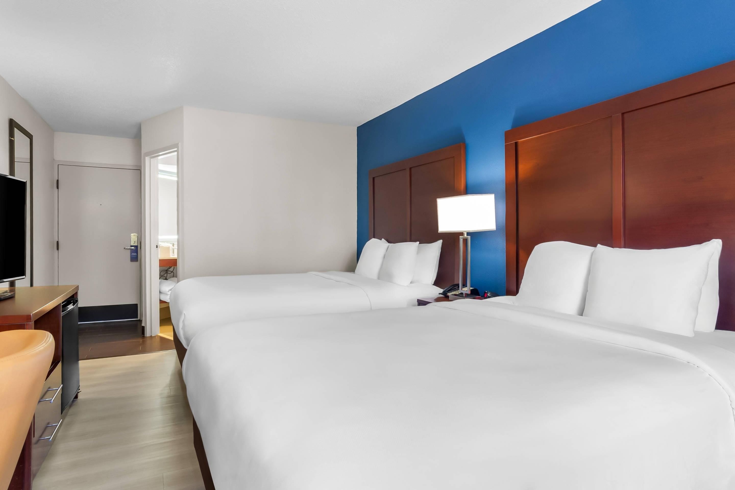 A hotel room with two beds, a desk, a TV, and a lamp.