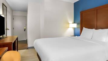 A hotel room with a large bed, a desk with a television, a chair, and a lamp.