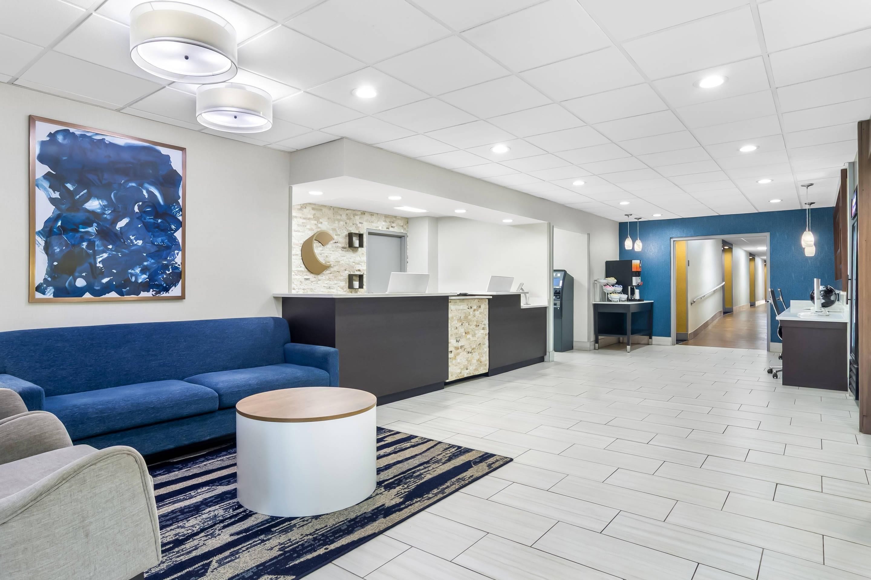 A modern hotel lobby with a blue sofa, a reception desk, and a large abstract painting.