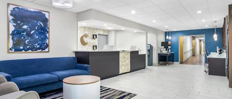 A modern hotel lobby with a blue sofa, a reception desk, and a large abstract painting.