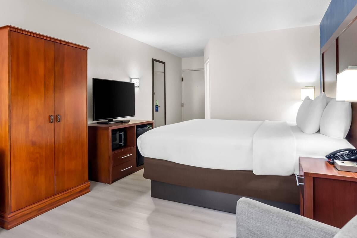 A hotel room with a large bed, a wardrobe, a television, and a desk with a telephone.