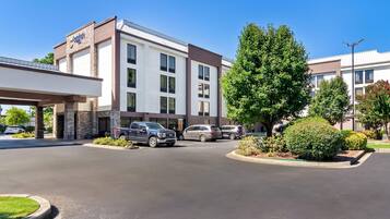 A hotel with a modern design, featuring a large parking lot and a covered entrance.