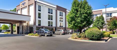 A hotel with a modern design, featuring a large parking lot and a covered entrance.