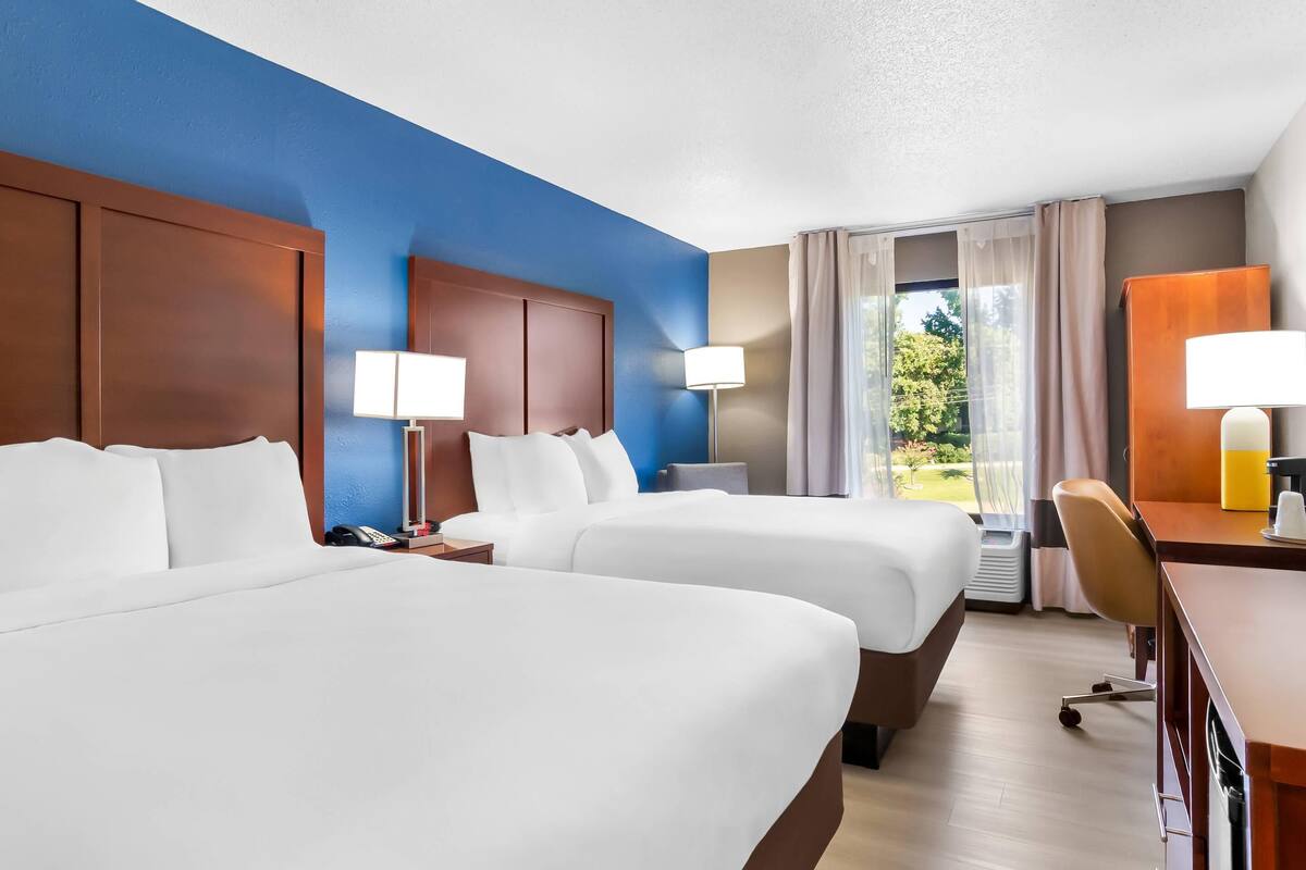 A hotel room with two beds, a desk, and a chair.