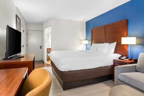 A hotel room with a large bed, a desk with a television, a chair, and a lamp. - Comfort Inn Greenville - Haywood Mall (Greenville)