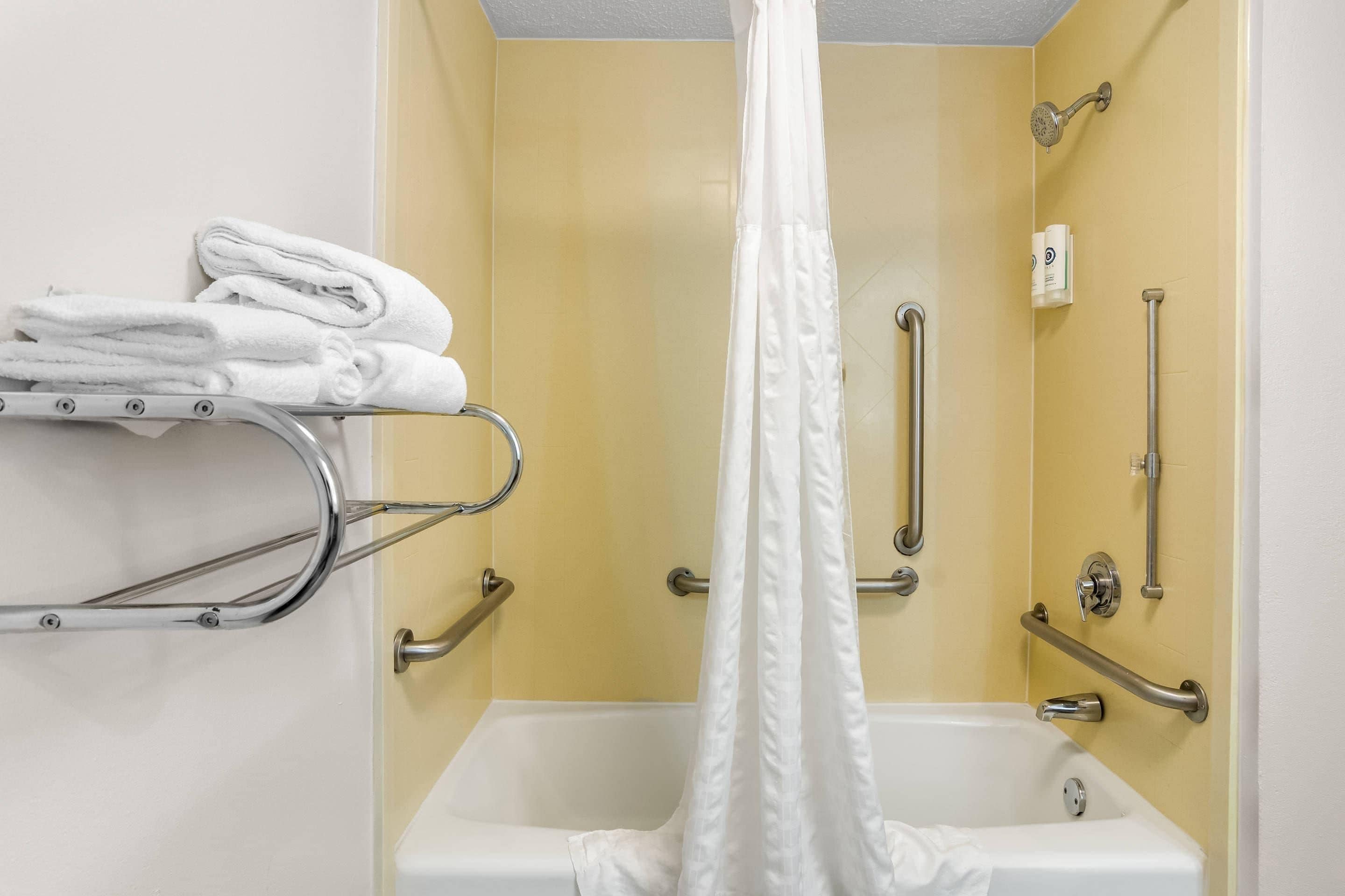 Un baño con bañera, ducha con cortina blanca y barras de apoyo.