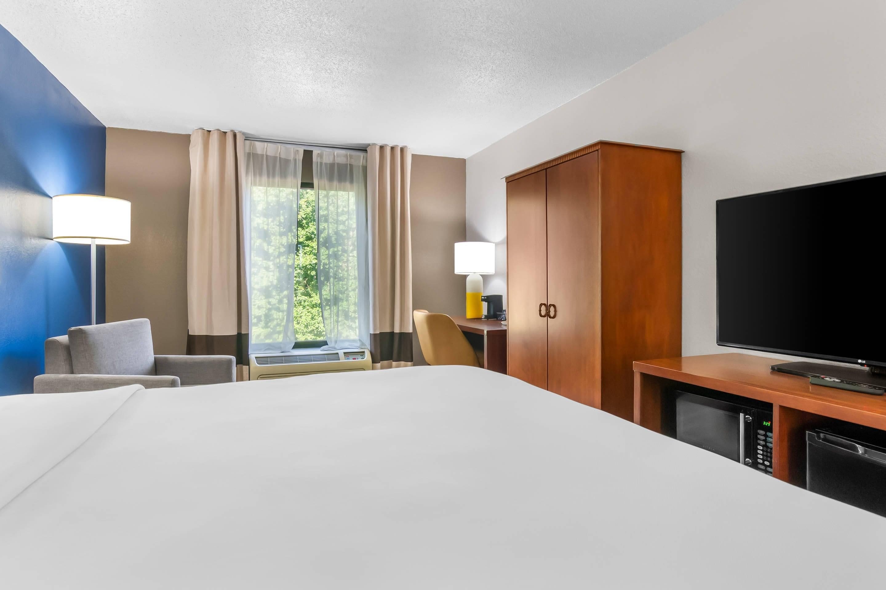 A hotel room with a large bed, a desk with a computer, a television, and a wardrobe.