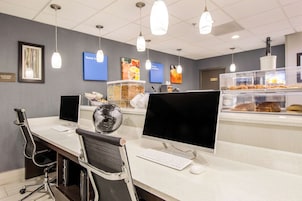 Zona de recepción de hotel con mostrador, computadoras, sillas y una vitrina con pasteles.