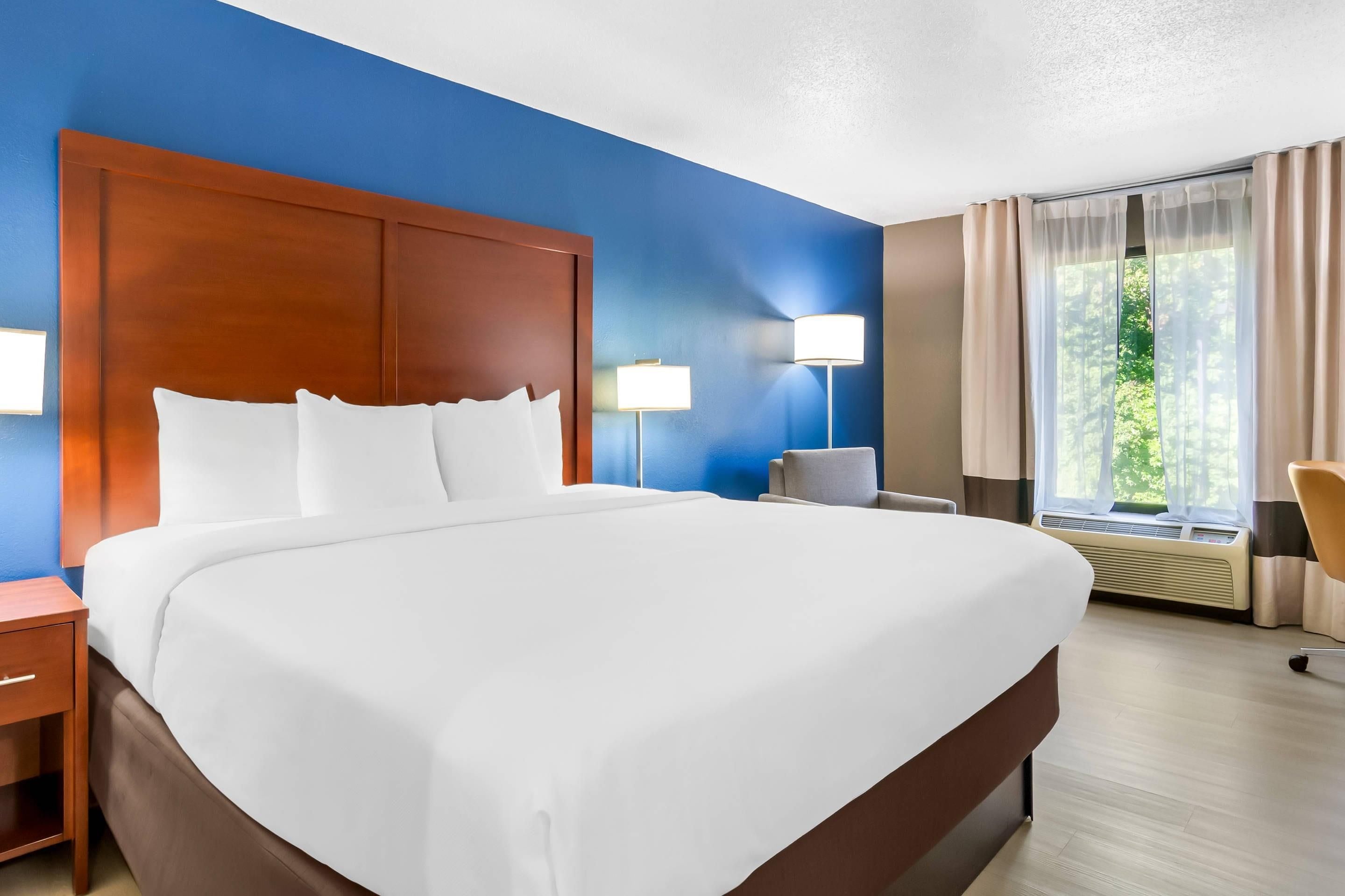 A hotel room with a large bed, two bedside lamps, a chair, and a window with curtains.