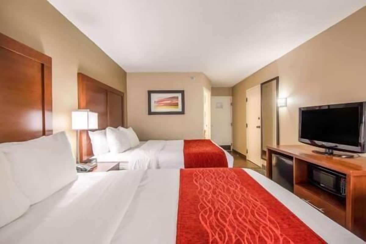 A hotel room with two beds, a TV, a desk, and a framed picture on the wall.