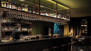 Zona de bar con diversas botellas de licores, una barra y varios taburetes.