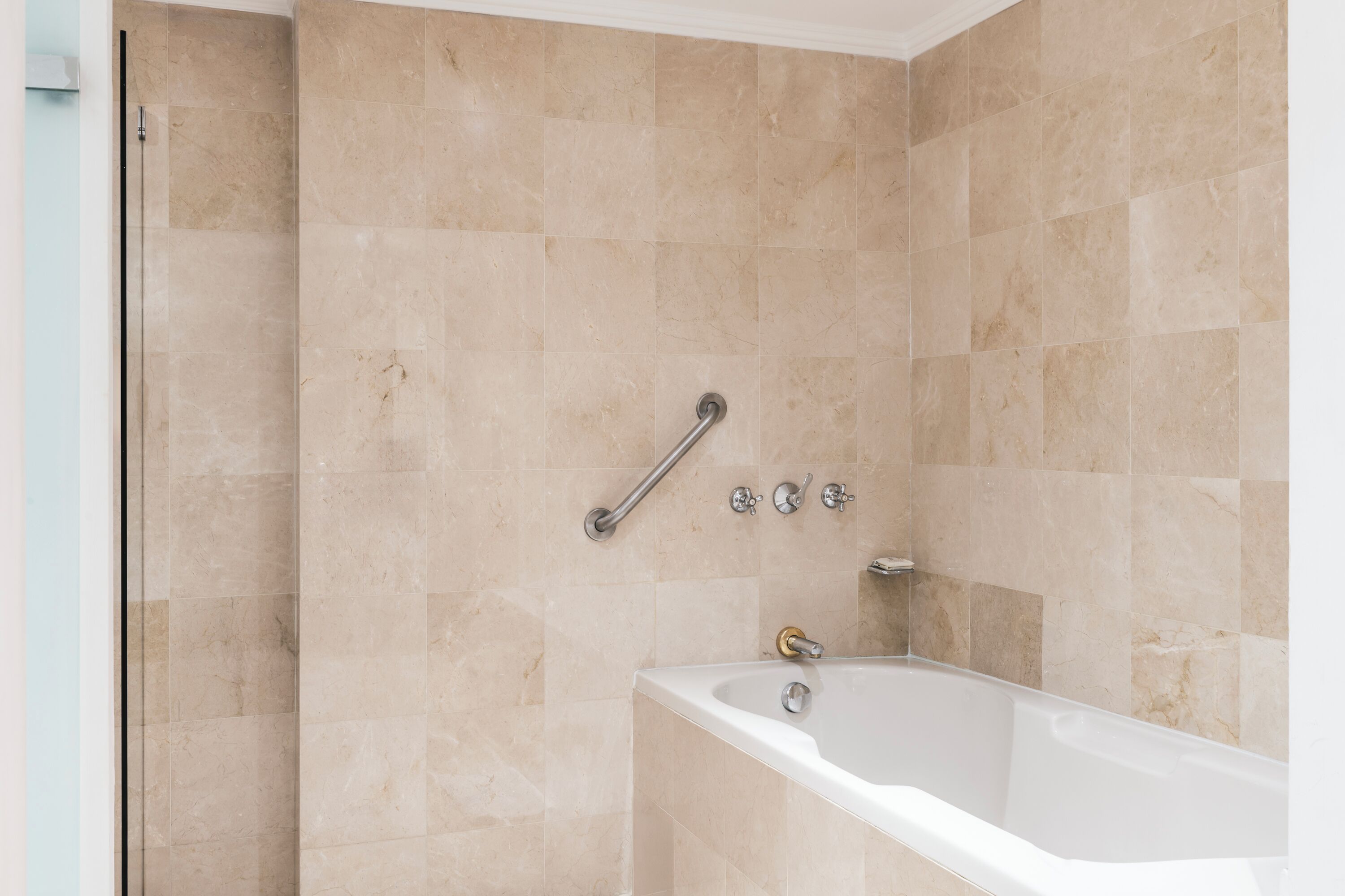 Un baño moderno con baldosas color beige, cabina de ducha a ras de suelo y bañera independiente.