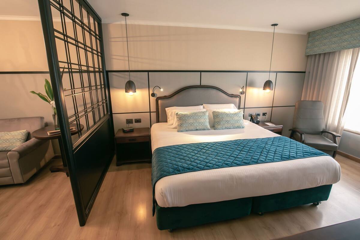 A modern hotel room with a large bed, two bedside tables, a chair, a desk, and a decorative screen.