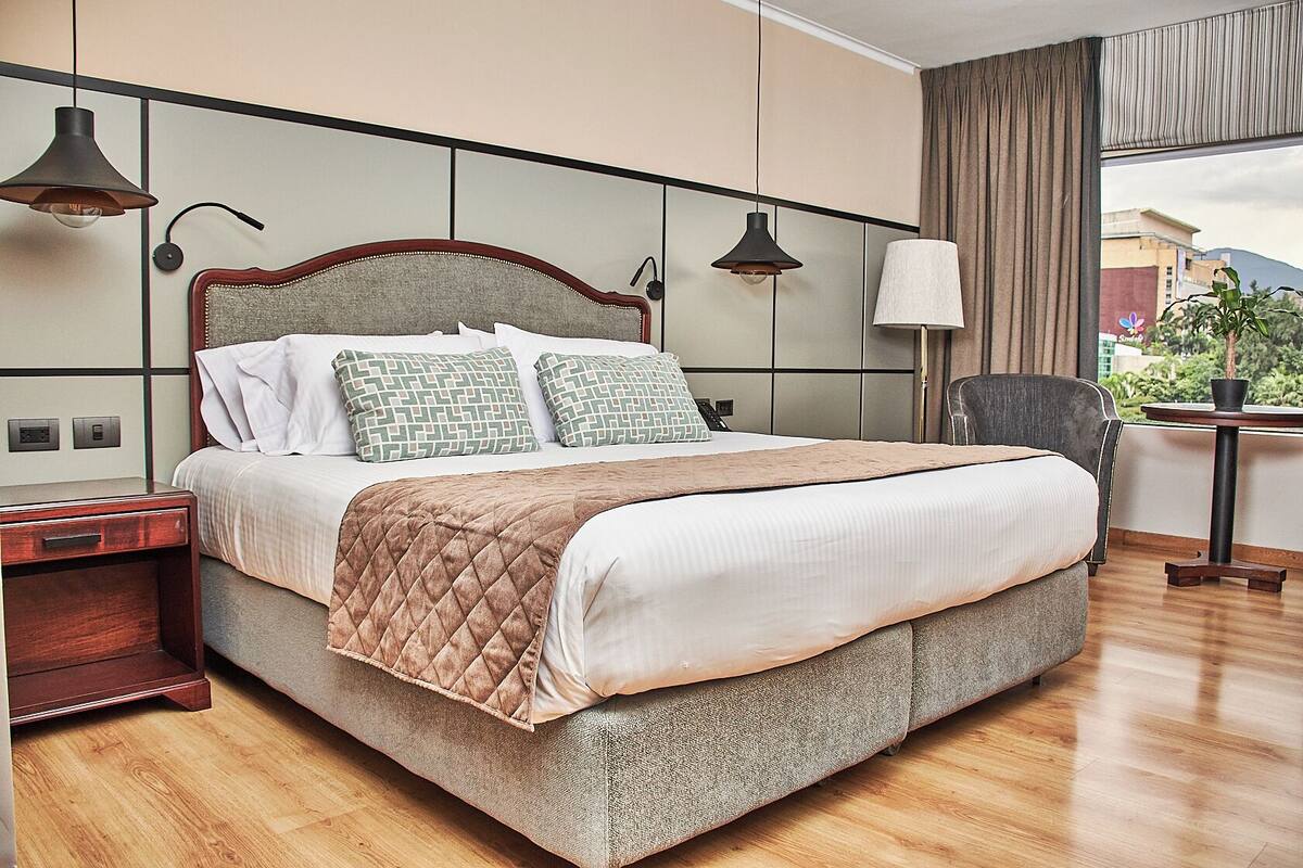 A neatly made bed with a quilted cover, a bedside table, and a chair.