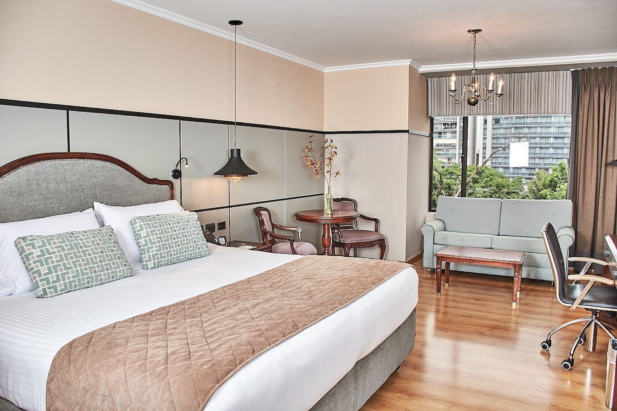 A hotel room with a large bed, a desk, a chair, a sofa, and a view of the city.