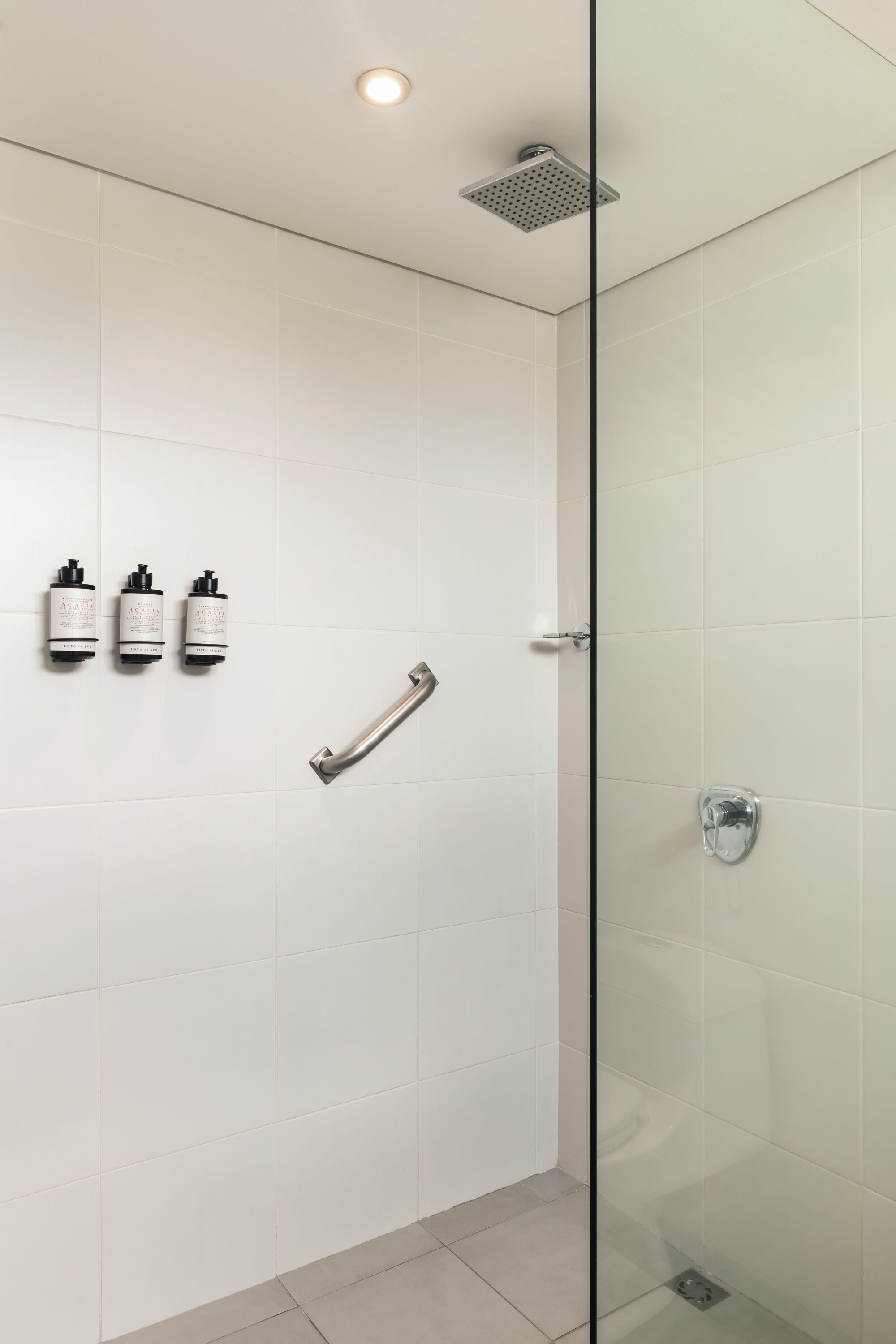 A modern bathroom with white tiles, a glass shower enclosure, and a handrail.