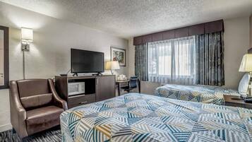 A hotel room with two beds, a TV, a desk, a chair, and a window with curtains.