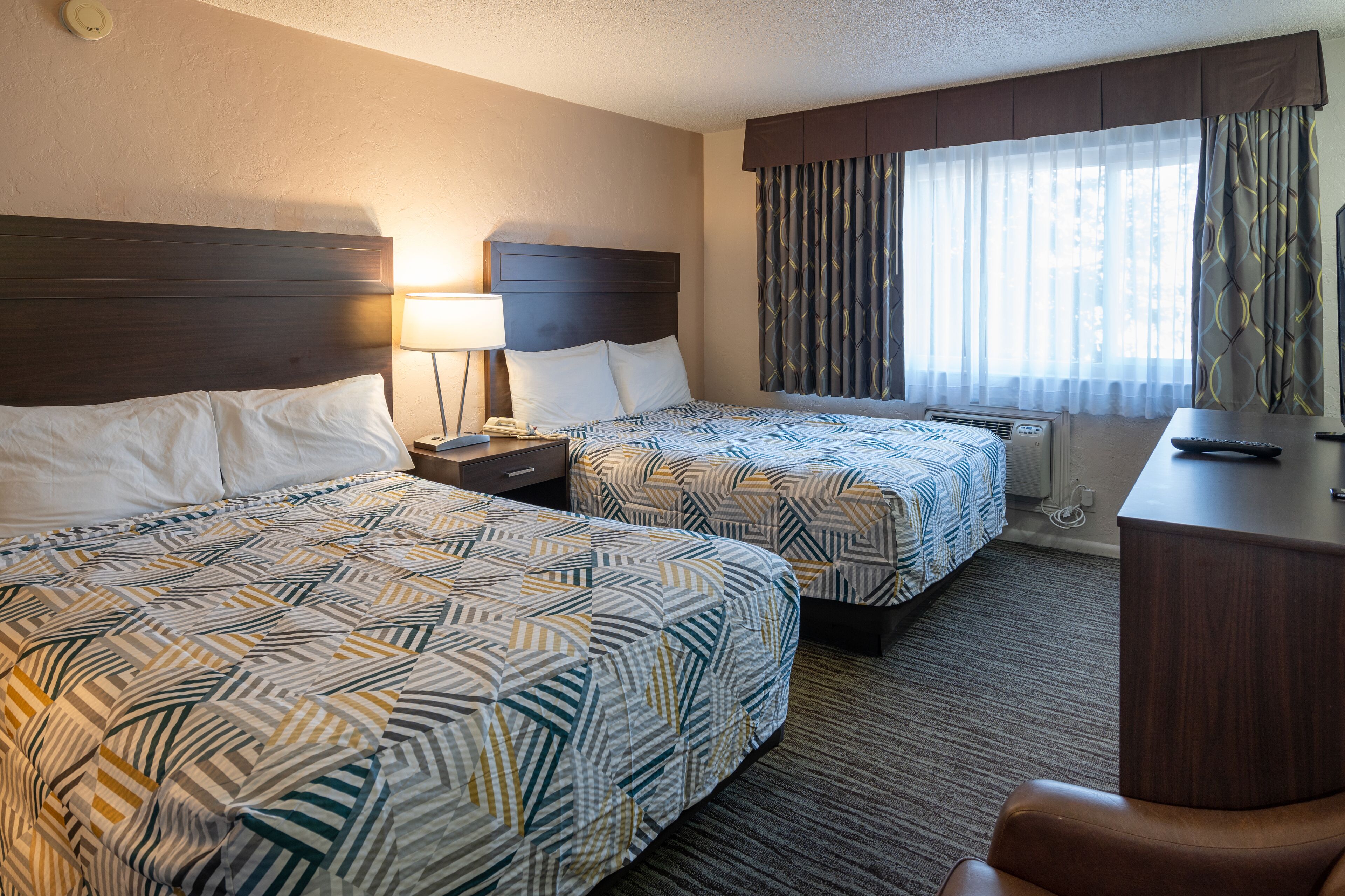 Habitación de hotel con dos camas, un escritorio, una silla, una lámpara y una ventana con cortinas.