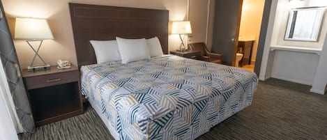 Een hotelkamer met een groot bed, twee nachtkastjes met lampen, een stoel en een raam.