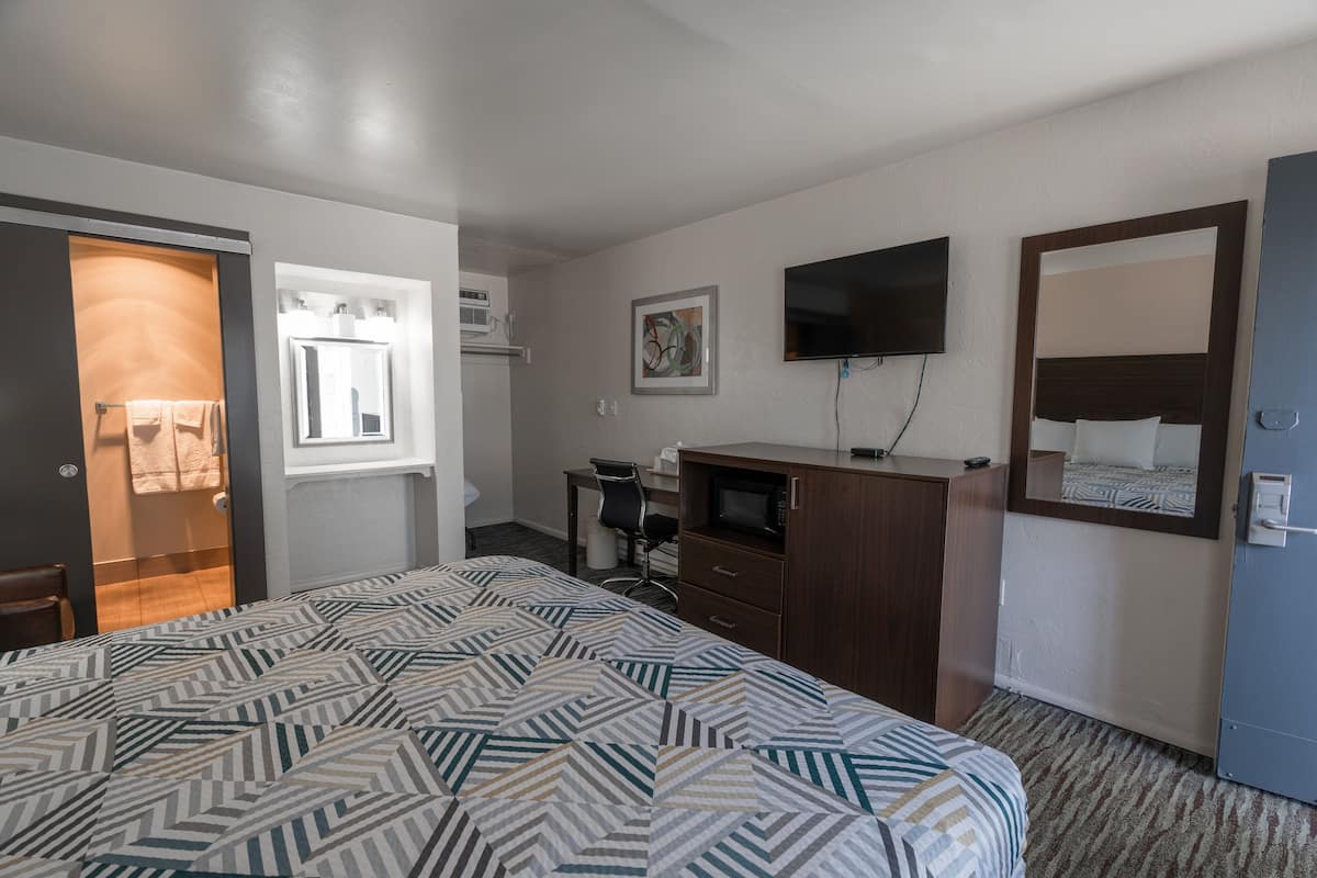 A hotel room with a large bed, a desk, a chair, a television, and a wardrobe.