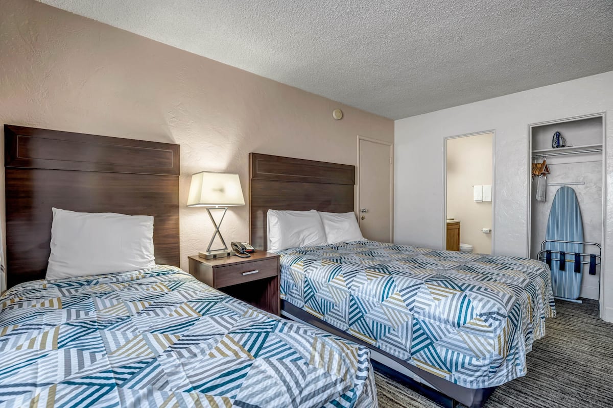 A hotel room with two beds, a nightstand with a lamp, a wardrobe, and a door leading to another room.
