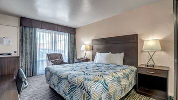 Habitación de hotel con una cama, dos mesitas de noche con lámparas, un escritorio, una silla y una ventana con cortinas.