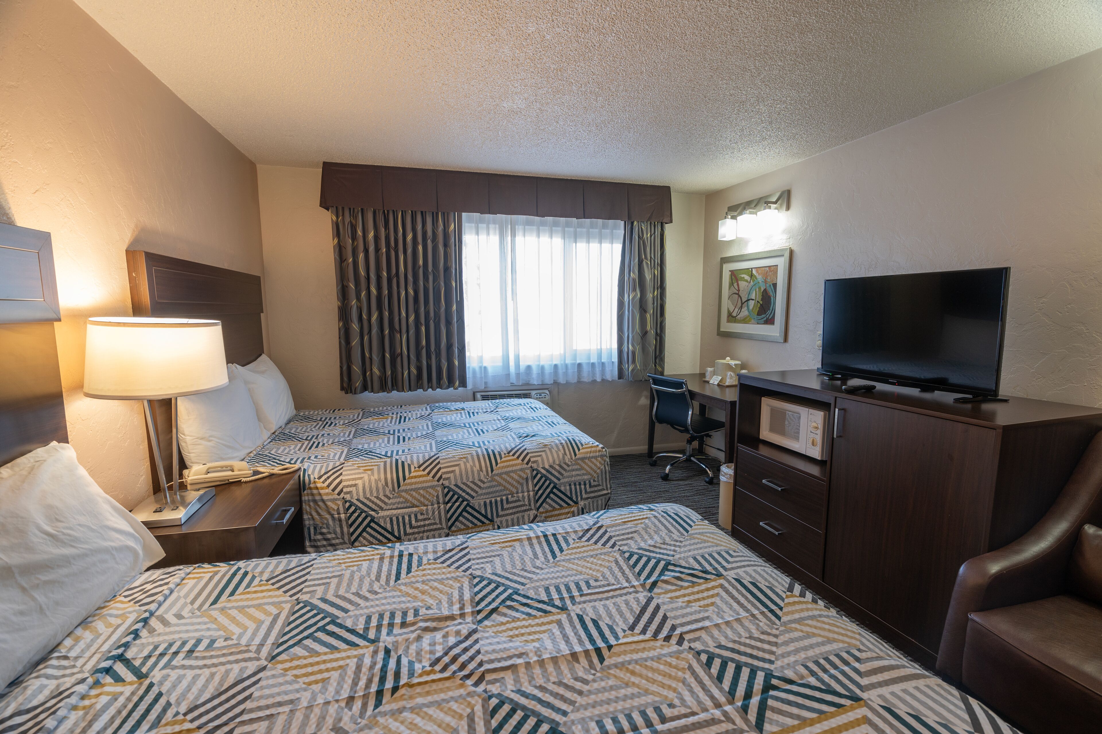A hotel room with two beds, a desk, a TV, and a chair.