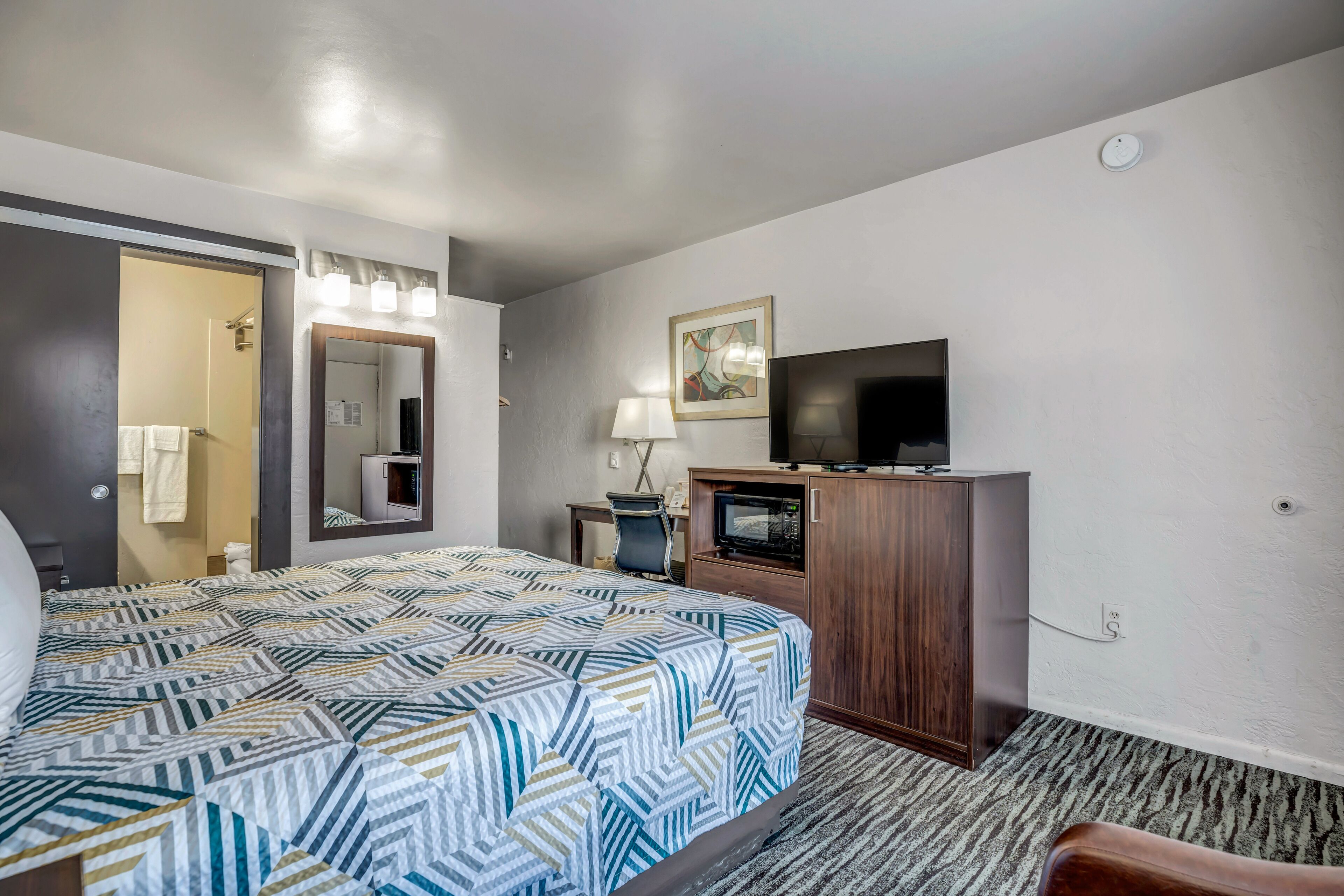 Een hotelkamer met een bed, een bureau, een televisie en een spiegel.