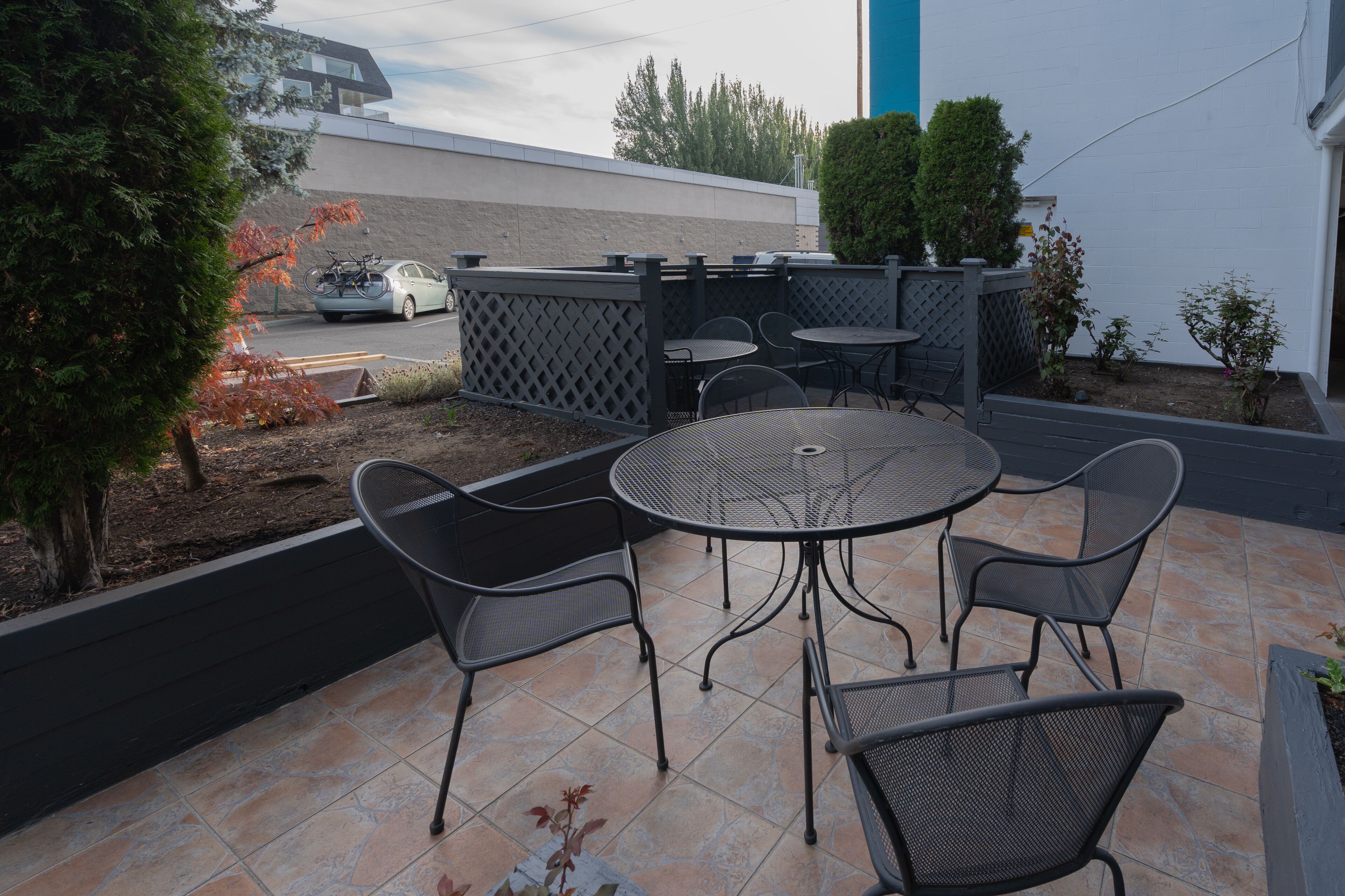 An outdoor patio with a round table and four chairs, surrounded by a low fence and small plants.