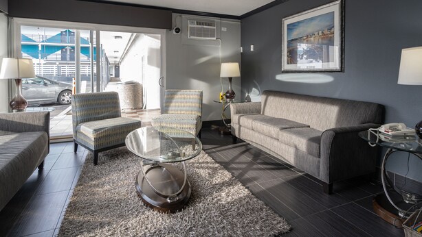 A modern living room with a sofa, armchairs, a glass coffee table, and a rug. There is a painting on the wall and a lamp on a side table.