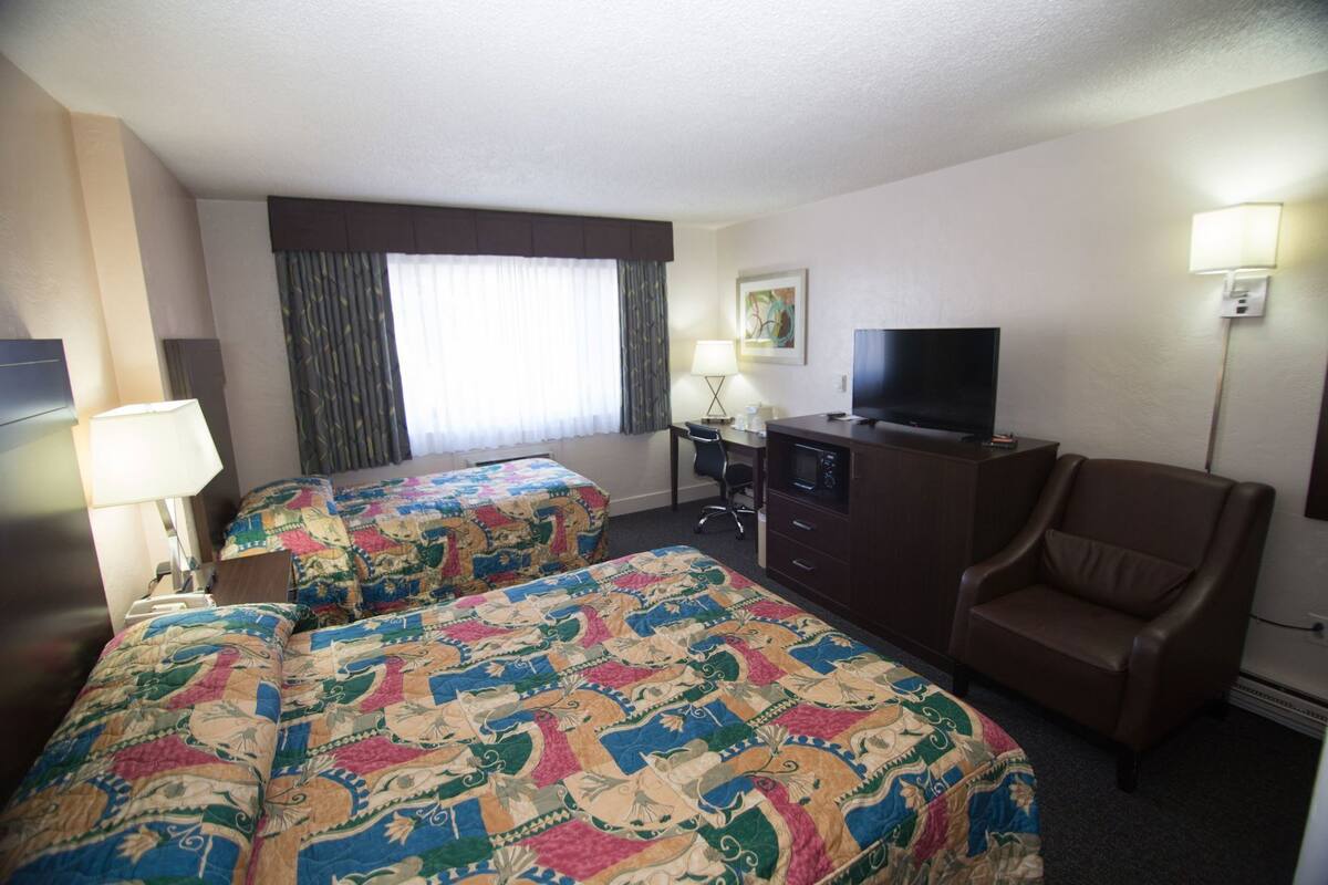 A hotel room with two beds, a TV, a desk, a chair, and a window with curtains.