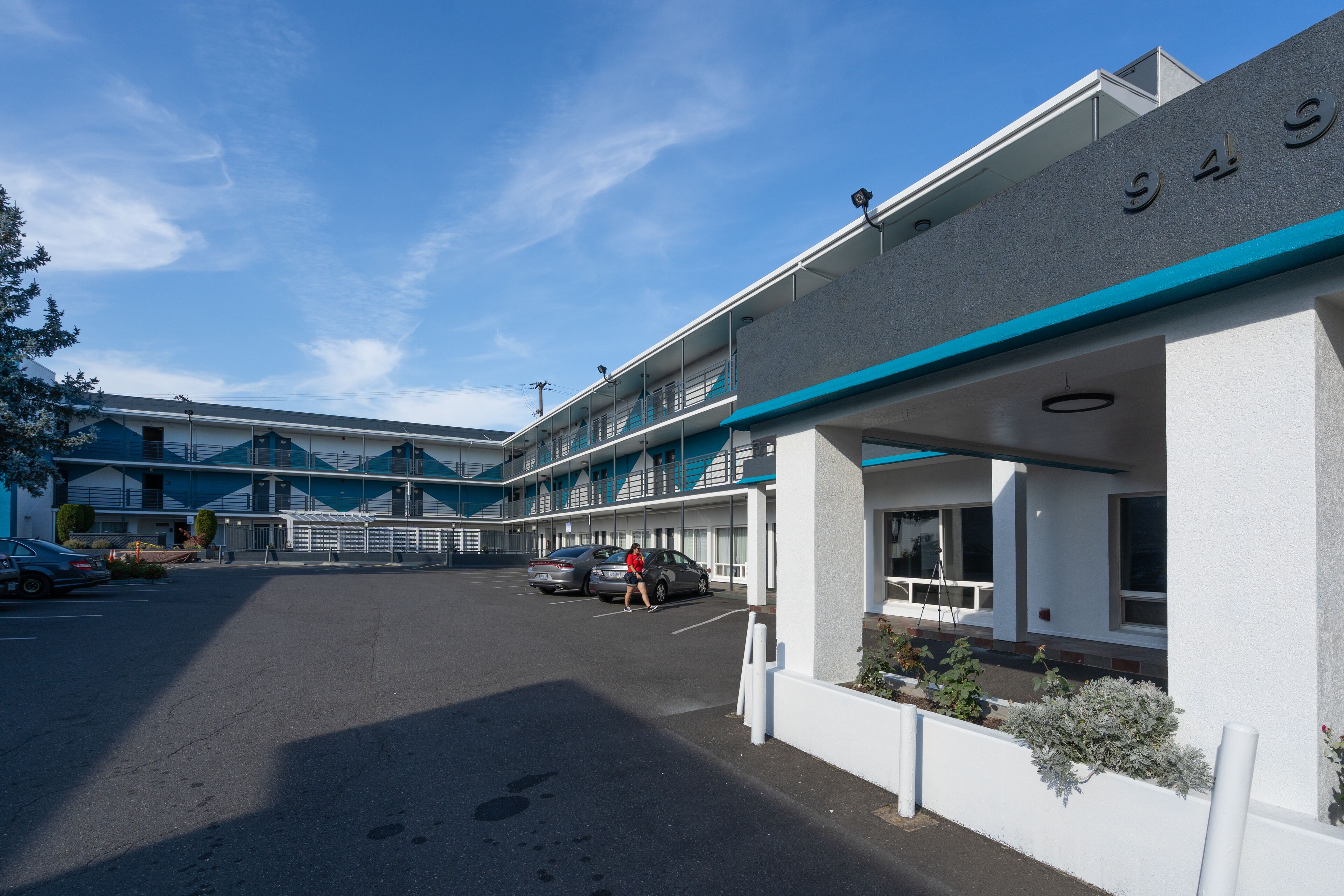 A motel with a parking lot, a building with a blue and white color scheme, and a sign with the number 945.