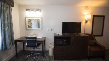 A hotel room with a desk, chair, television, and a small cabinet.