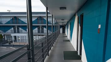 A corridor with a metal railing, a blue wall, and a building with a blue and white facade in the background.