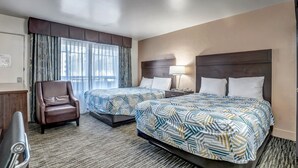 A hotel room with two beds, a desk, a chair, and a window with curtains.