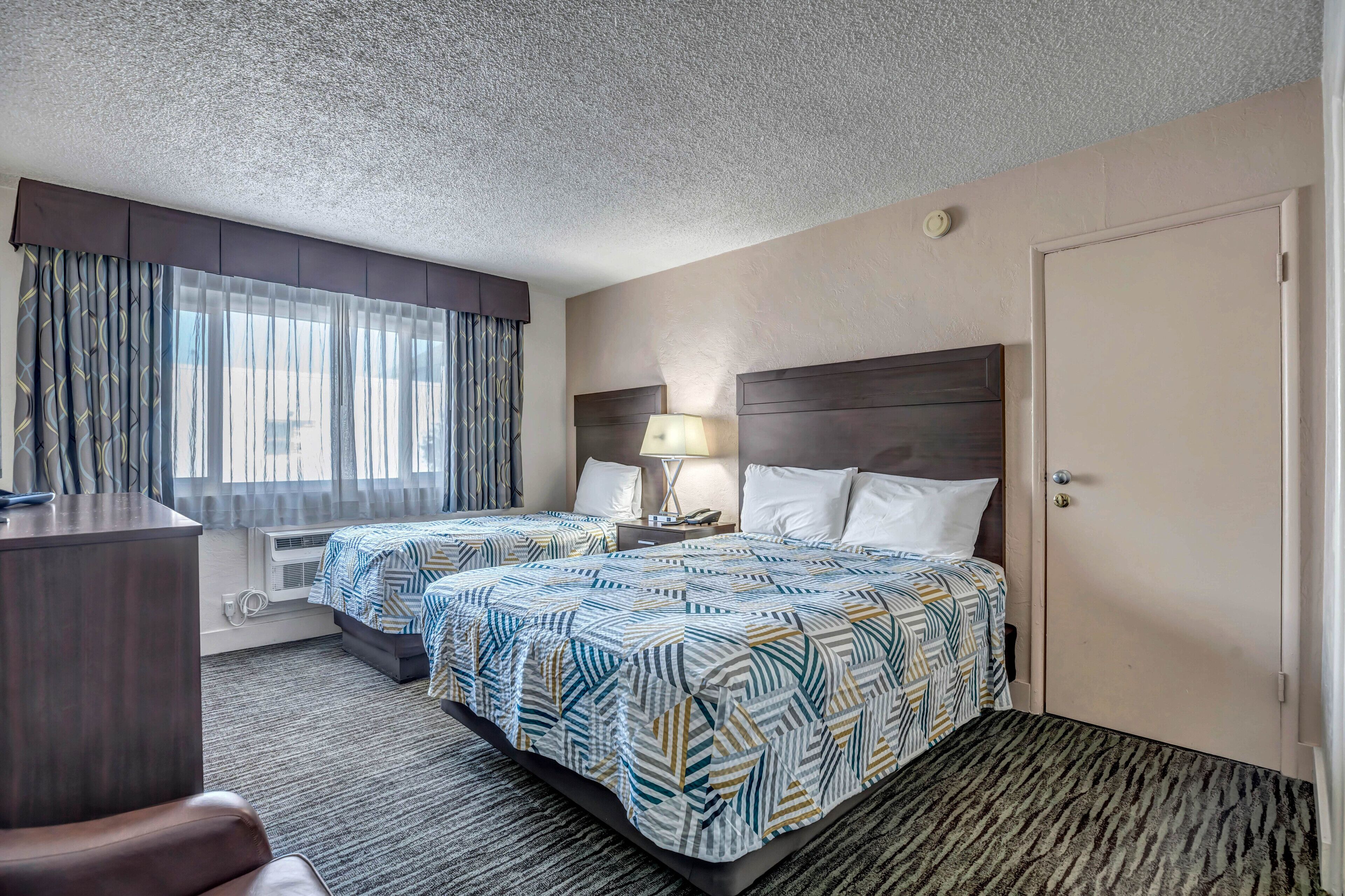 Een hotelkamer met twee bedden, een bureau, een lamp en een deur.