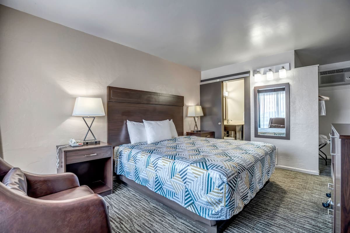 A hotel room with a large bed, two bedside tables with lamps, a brown leather chair, a walk-in closet, and a mirror above the bed.
