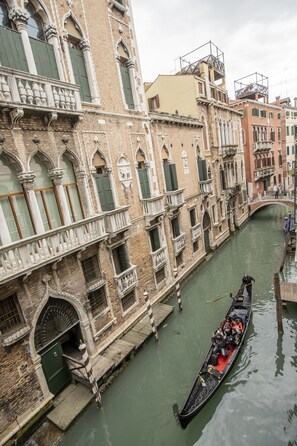 A narrow canal with a gondola filled with passengers, surrounded by historic buildings with ornate facades and green shutters. - Hotel Ateneo (Venice)