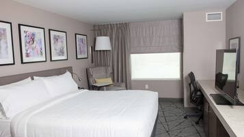 Een hotelkamer met een groot bed, een bureau met een computer, een stoel en een raam met gordijnen.